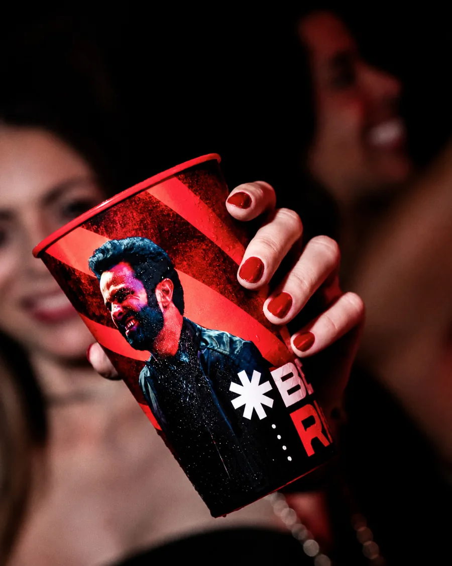 Mão segurando um copo vermelho com a foto de um cantor impressa em volta