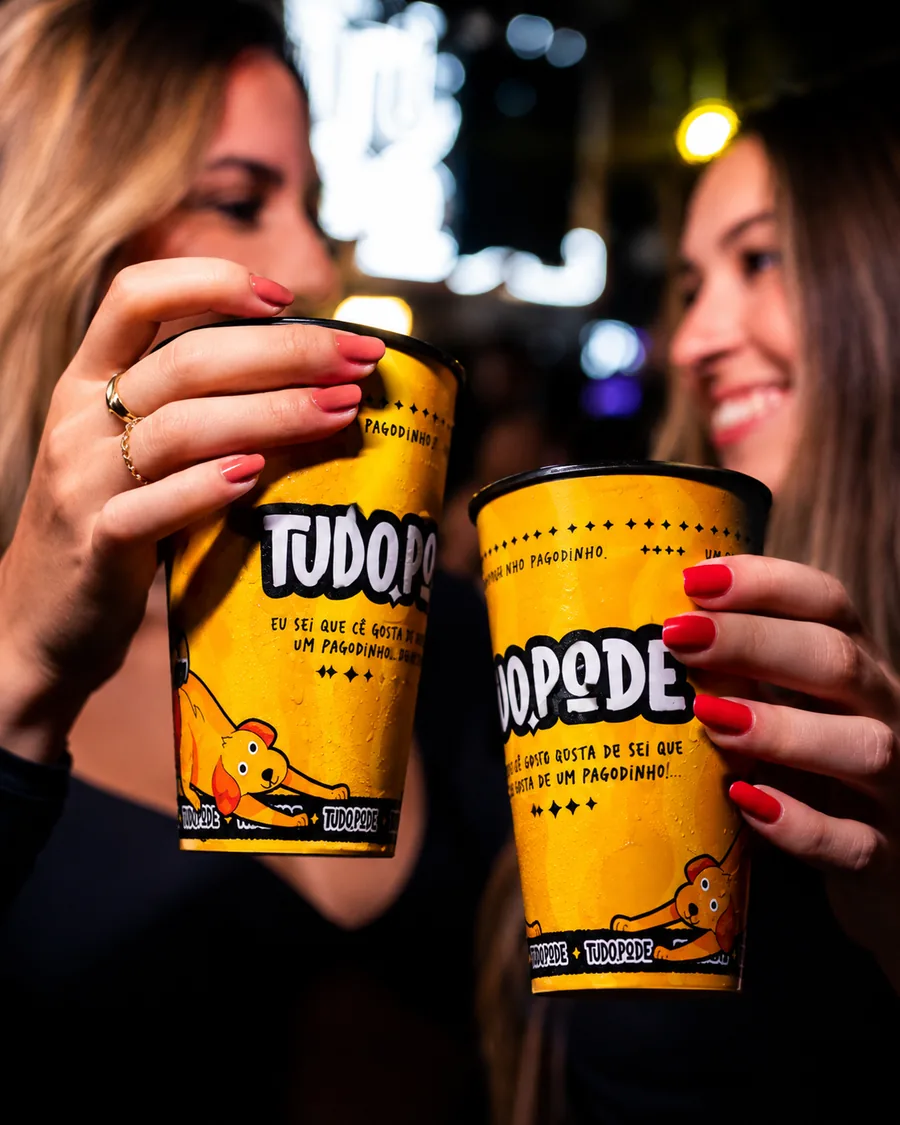 Duas amigas brindando com copos amarelos Tudo Pode em um show